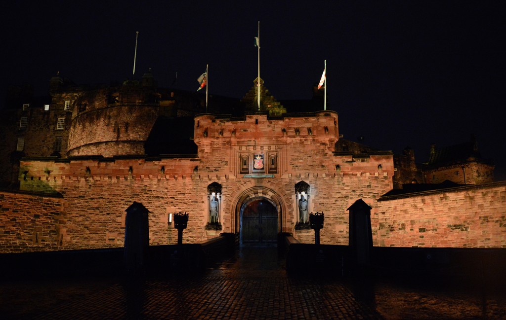 Murs de l'entrée du château, éclairés par le bas, dans la nuit, avec une allée pavée y menant