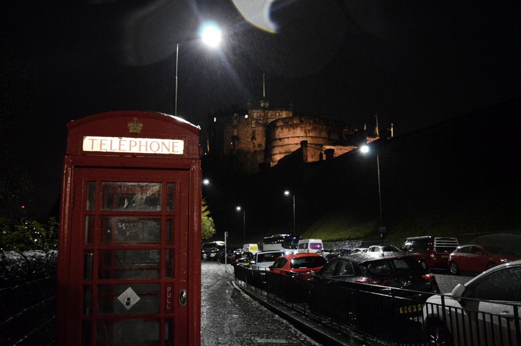 Cabine rouge de téléphone au premier plan, avec le château éclairé en arrière plan, perché sur sa colline