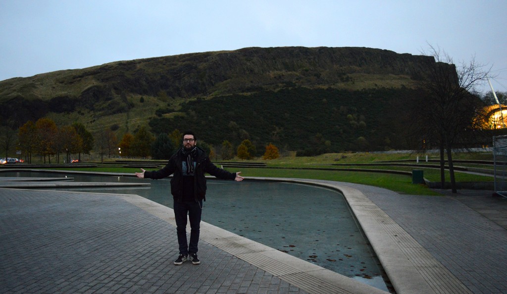 Manu debout sur la place de Holyroodhouse, avec la colline d'Arthur's seat en arrière plan