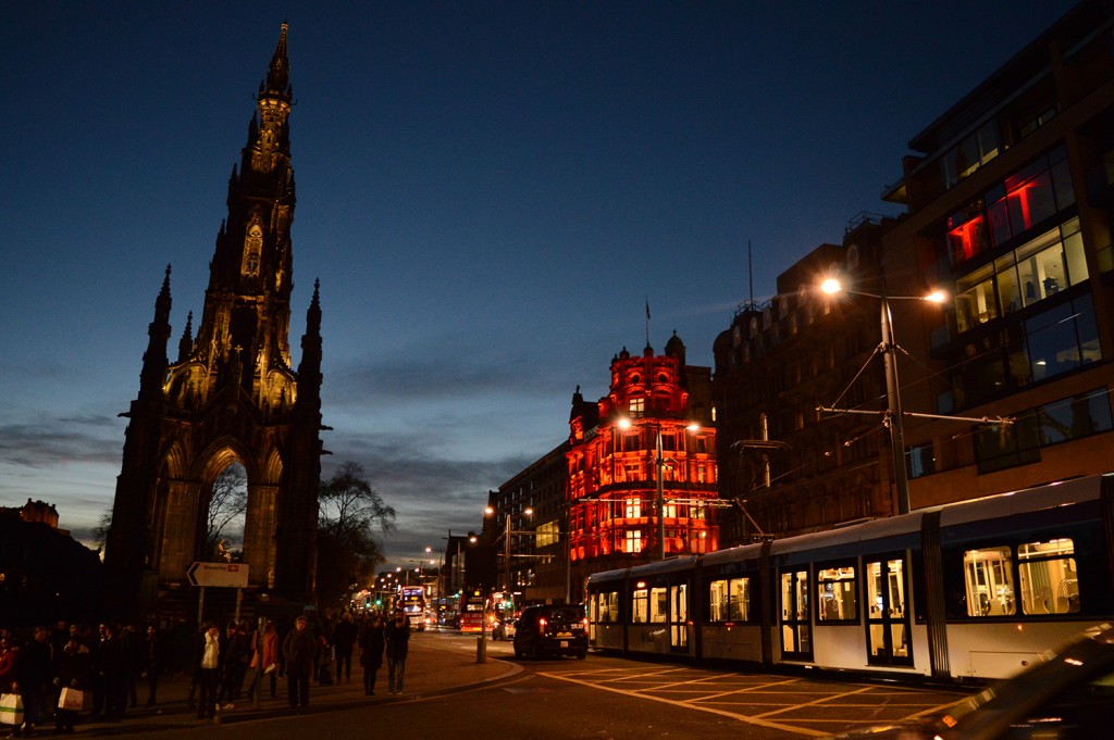 Rue éclairée de nuit avec façade rouge à droite, du aux éclairages, et le Scott Monument à gauche