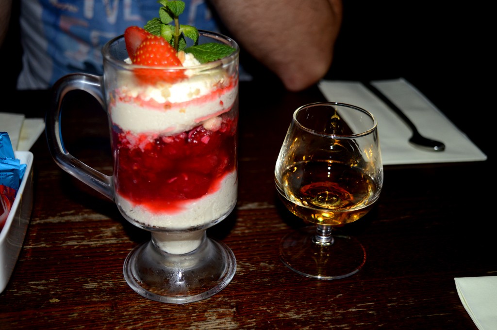 Dessert à la crème et aux fruits rouges, dans un verre, à côté d'un petit verre de whisky