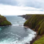 Un littoral avec des falaises abruptes au-dessus de l'océan. Les vagues s'écrasent contre les rochers, appelés Duncansby Stacks
