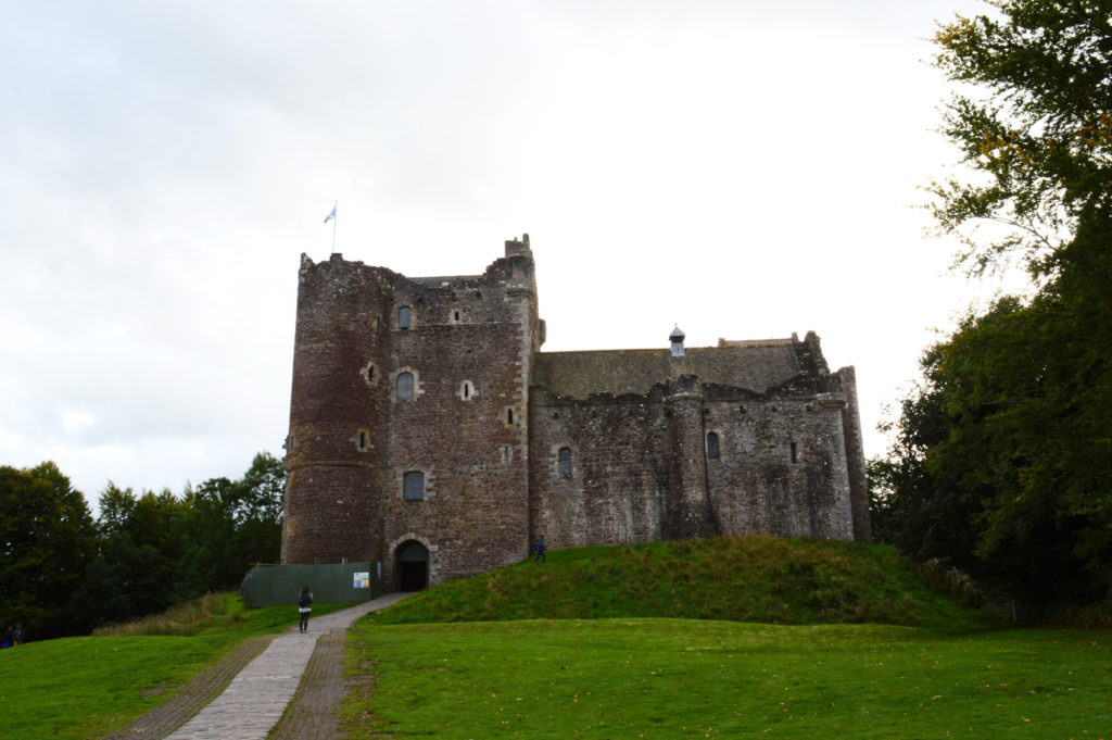 Chateau de doune, en vieilles pierres recouvertes de mousse. Pelouse verte au premier plan