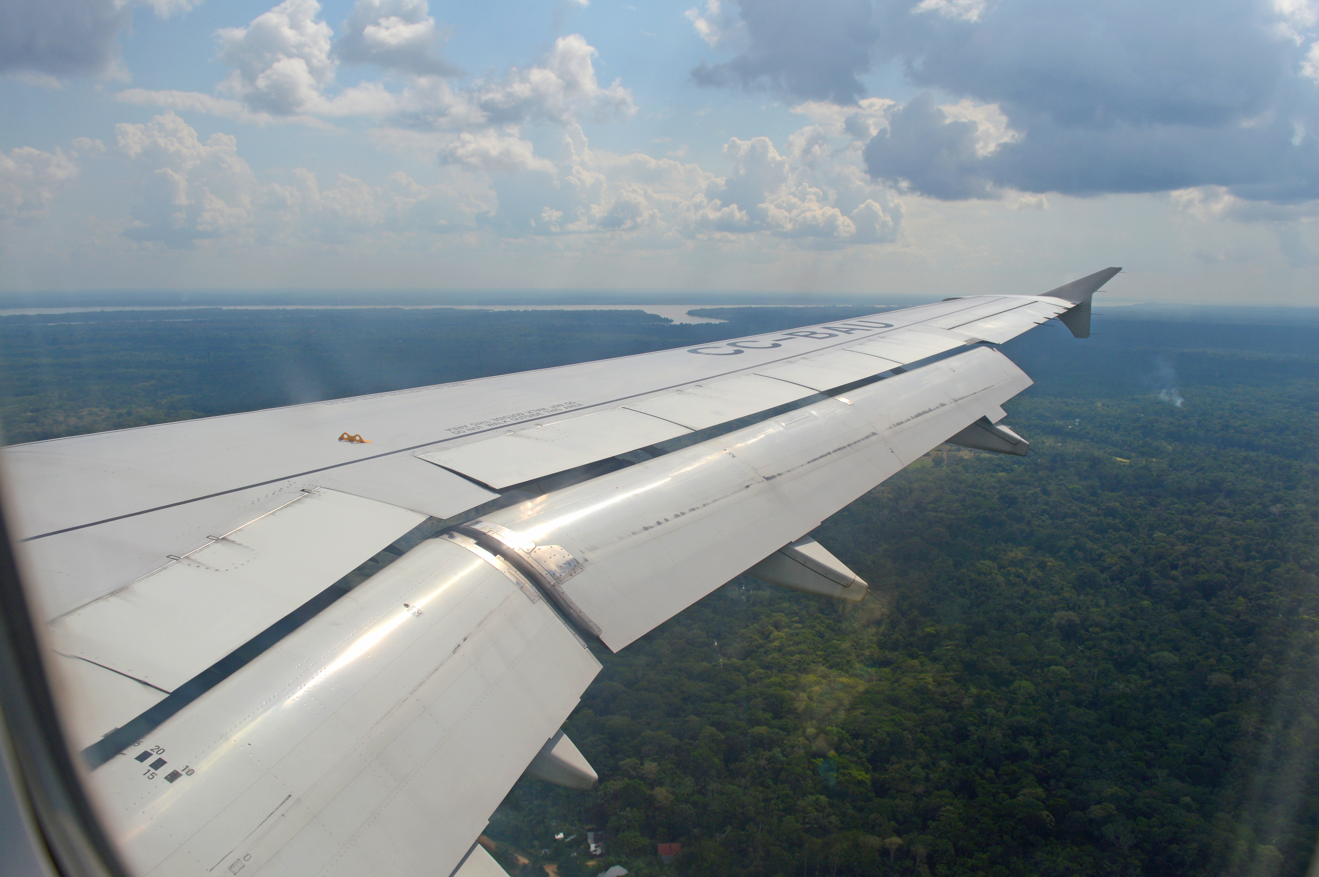 Aile d'un avion depuis le hublot, au dessus de la canopée de l'Amazonie, et du fleuve amazone au loin
