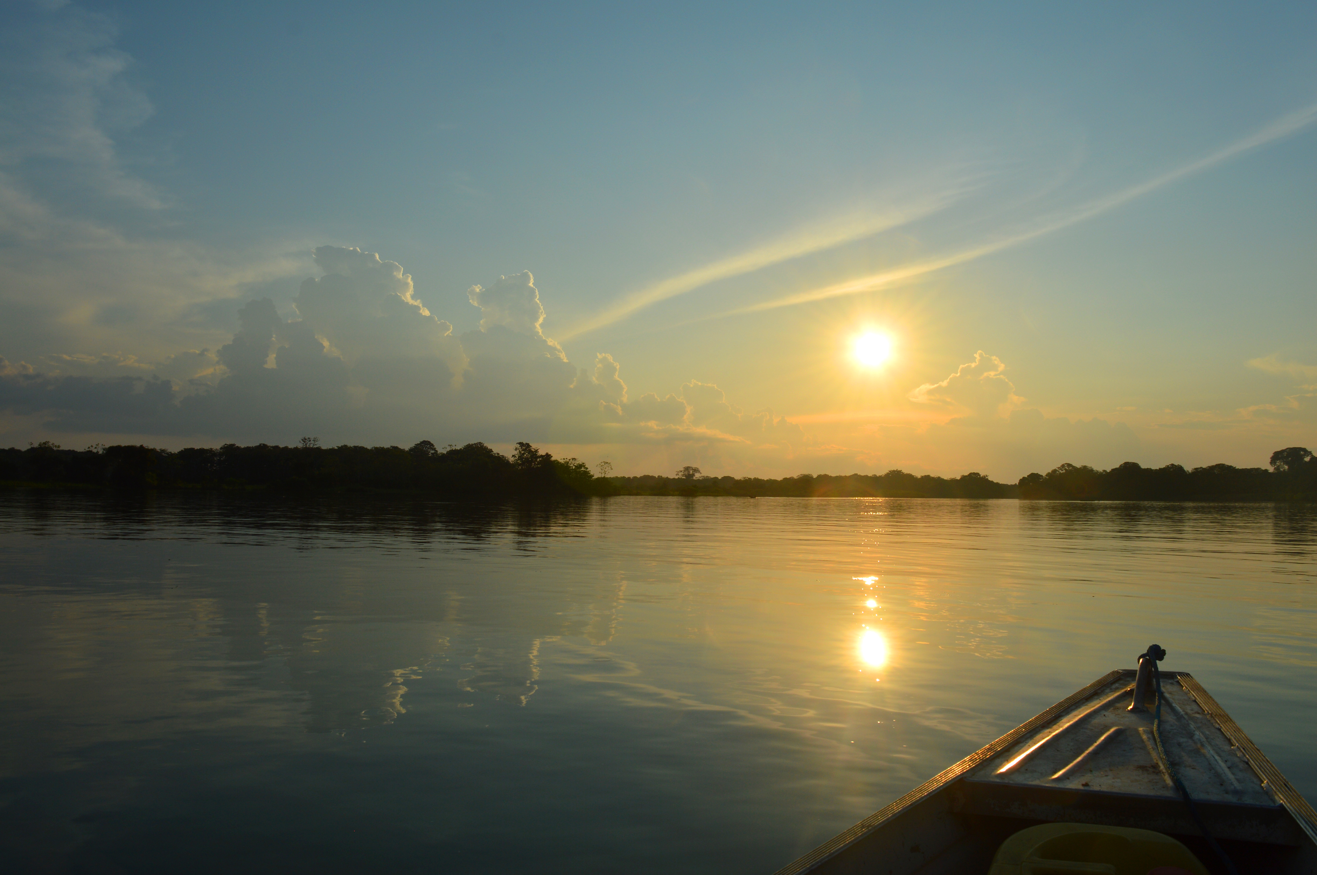 Soleil couchant au dessus de l'horizon, se reflétant sur l'Amazone, avec la pointe de la barque dépassant du bas de la photo