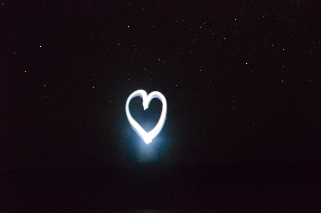 Cœur dessiné par la lumière du téléphone, grâce à une pause longue, avec le ciel étoilé en fond