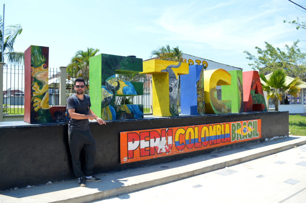 Manu devant les lettres multicolores de la décoration à l'entrée de la ville : "Leticia - Peru Colombia Brasil"