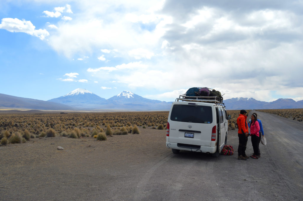 Van garé en bord d'une route de terre, à l'entrée du parc national Sajama, avec les volcans Parinacota et Pomerape en arrière plan