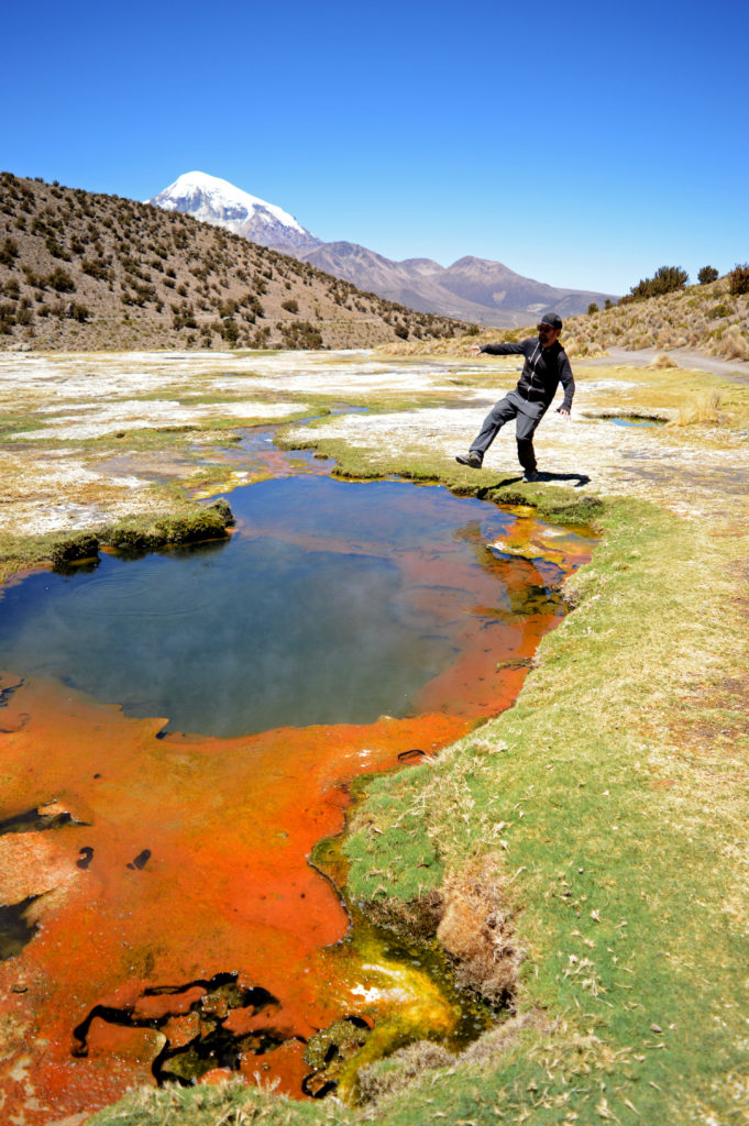 Geyser teinté d'une couleur orange. Le sommet enneigé du volcan dépasse en arrière plan