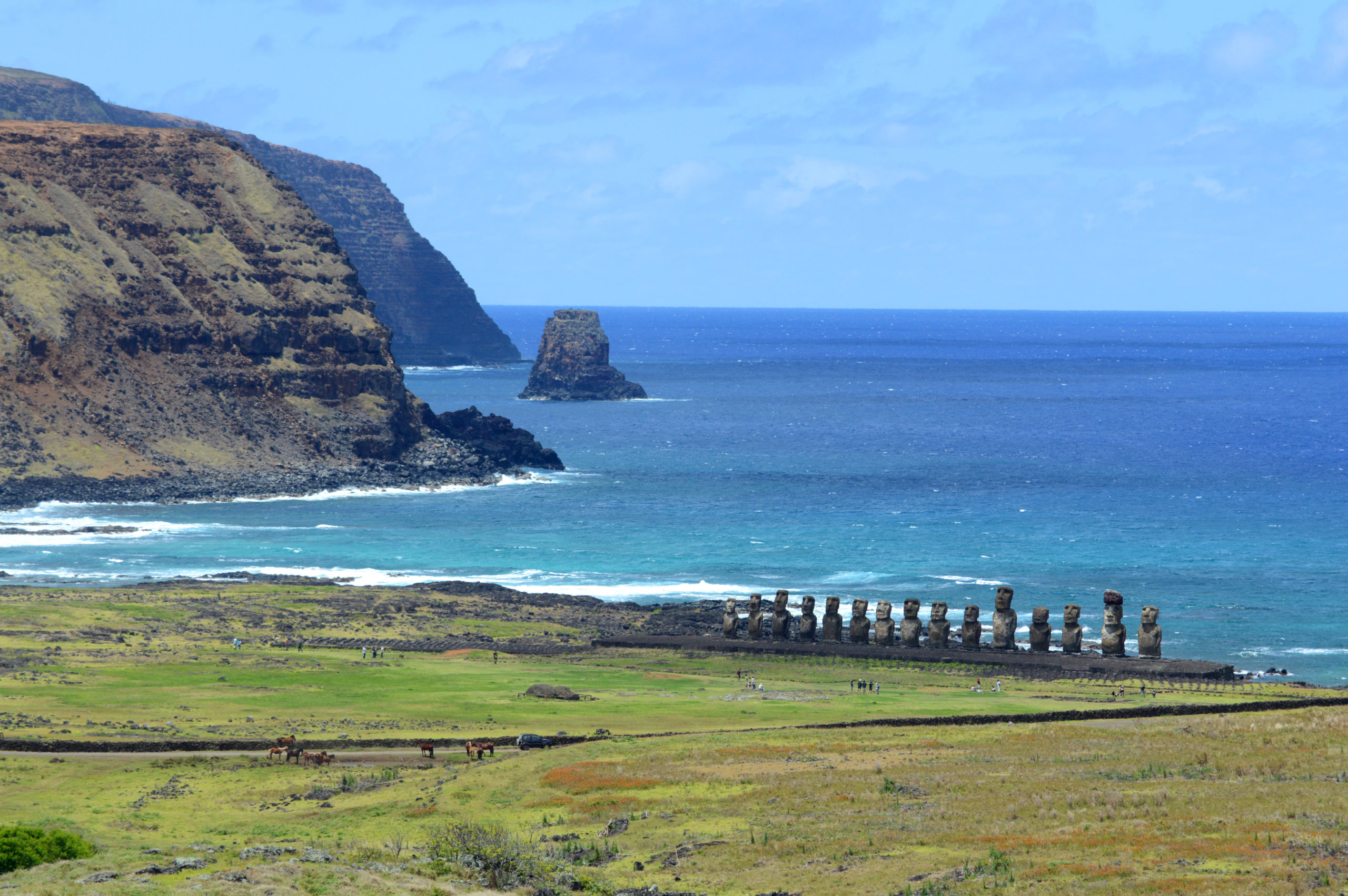 Vue sur les immenses falaises noires au loin, et en contre bas, sur les statues de Tongariki, alignées, dos à l'océan