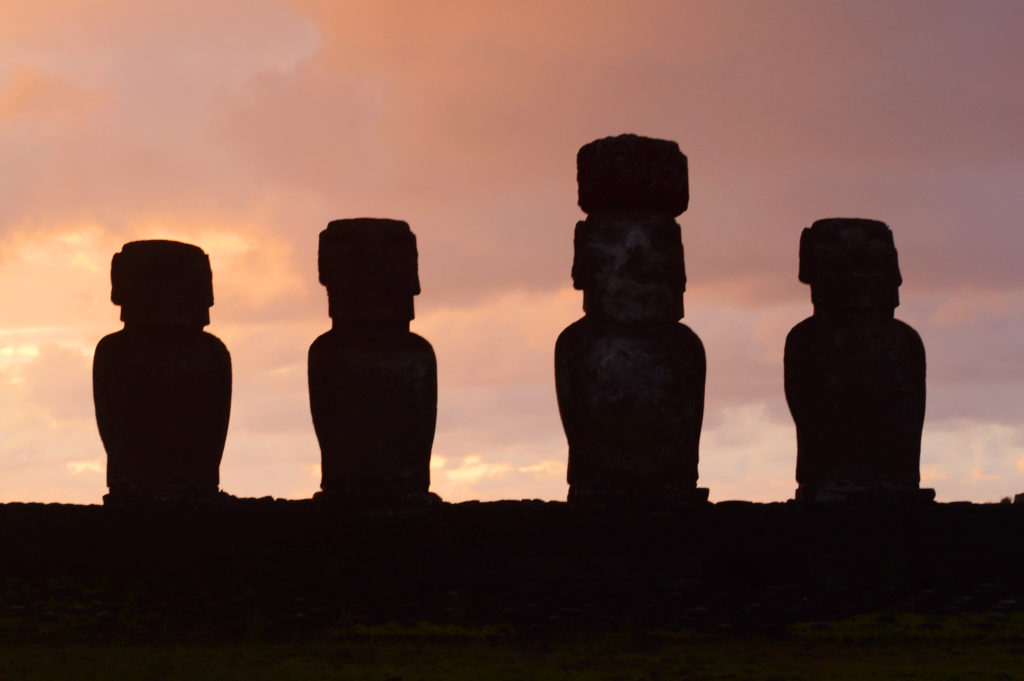 4 statues en contre jour, paraissant toutes noires, devant le ciel rouge du soleil levant