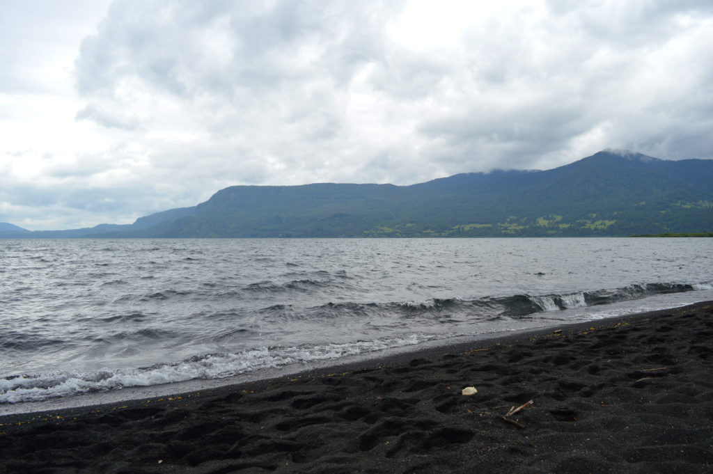 Eau grise et agitée d'un lac aux plages de sable noir