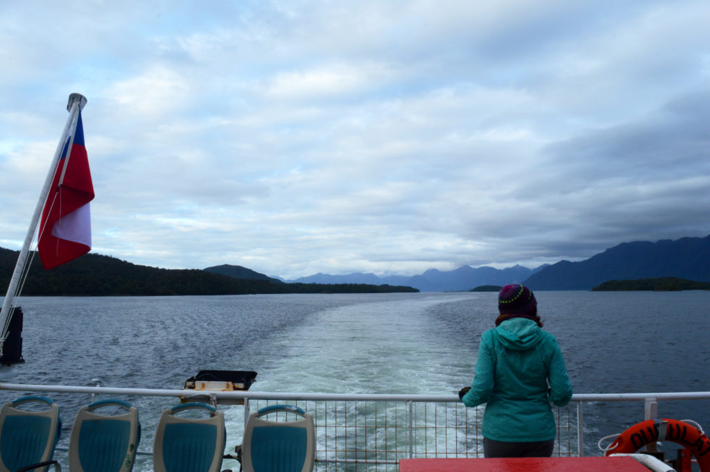 Amandine de dos, se tenant à la rambarde arrière du ferry, admirant les montagnes et ilots des fjords