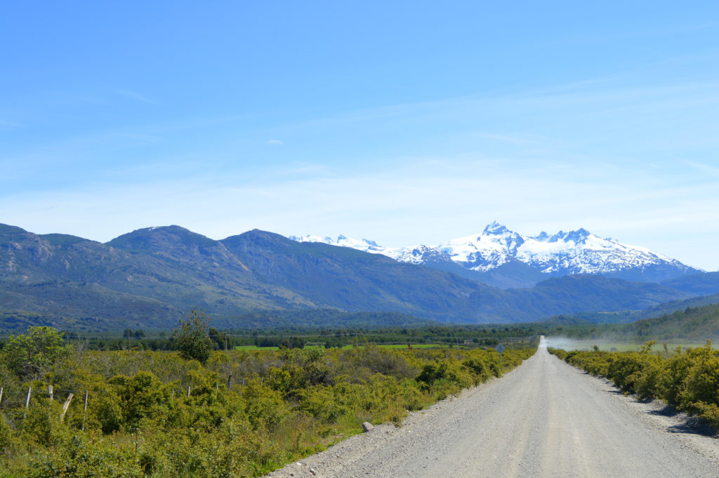 Route de cailloux de la carretera austral en Patagonie, traversant une végétation verte, et emmenant droit avec des sommets enneigés au loin
