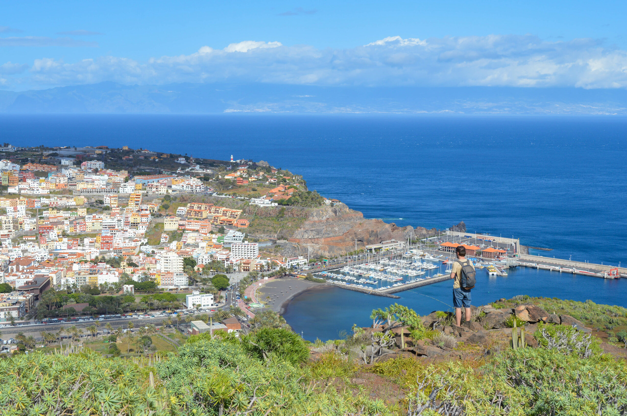 Manu debout, en bord de falaise, observant la vue en contrebas sur le port et la ville de San Sebastian de La Gomera