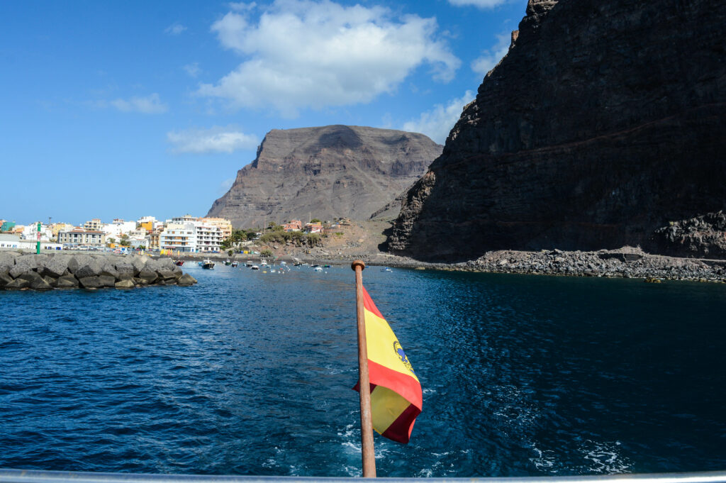 Drapeau espagnol flottant à l'arrière d'un bateau sur l'océan, avec vue sur La Gomera et ses falaises, au loin
