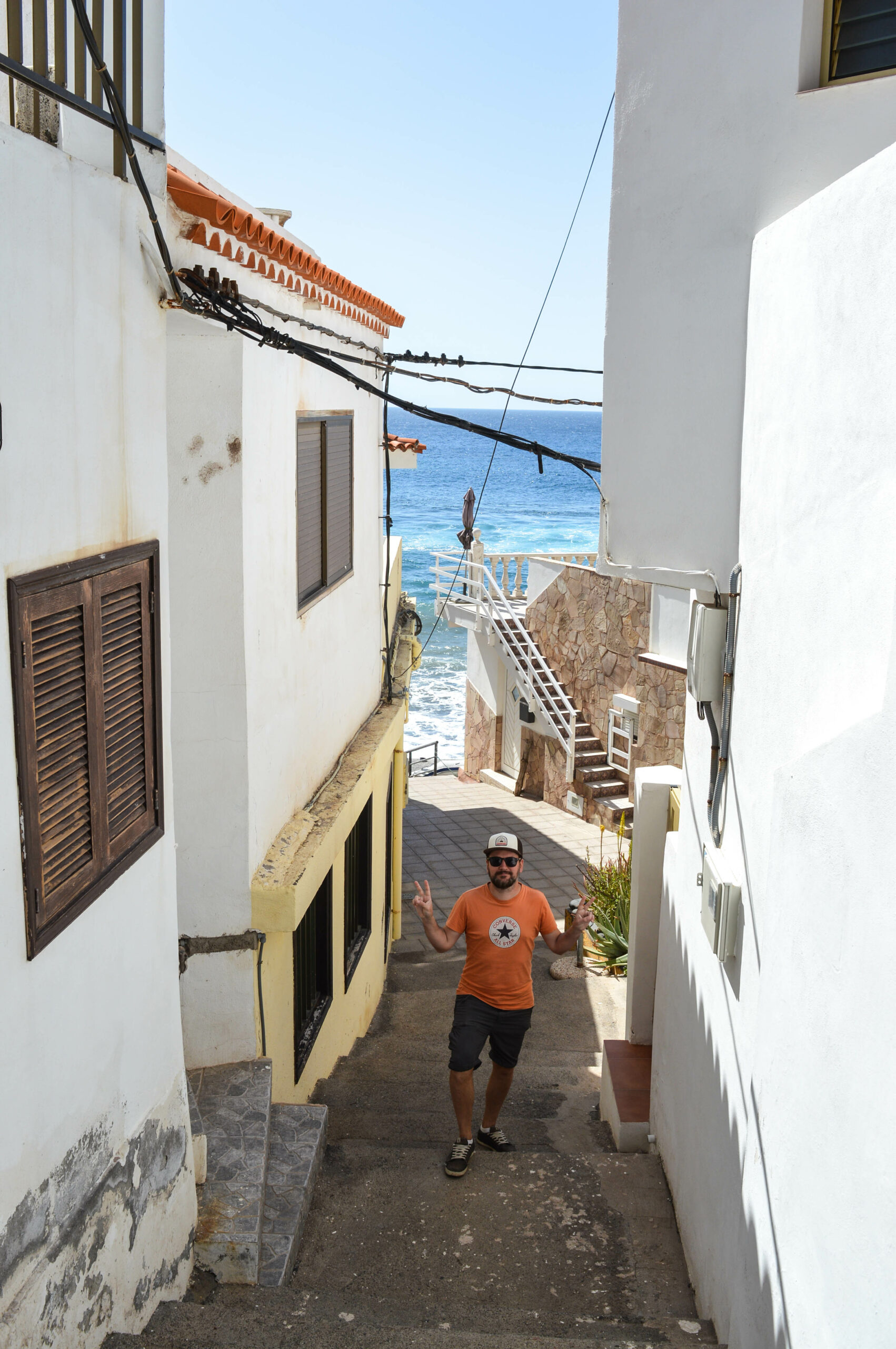 Manu dans des escaliers d'une ruelle aux maisons blanches d'Alojera, emmenant vers l'océan 