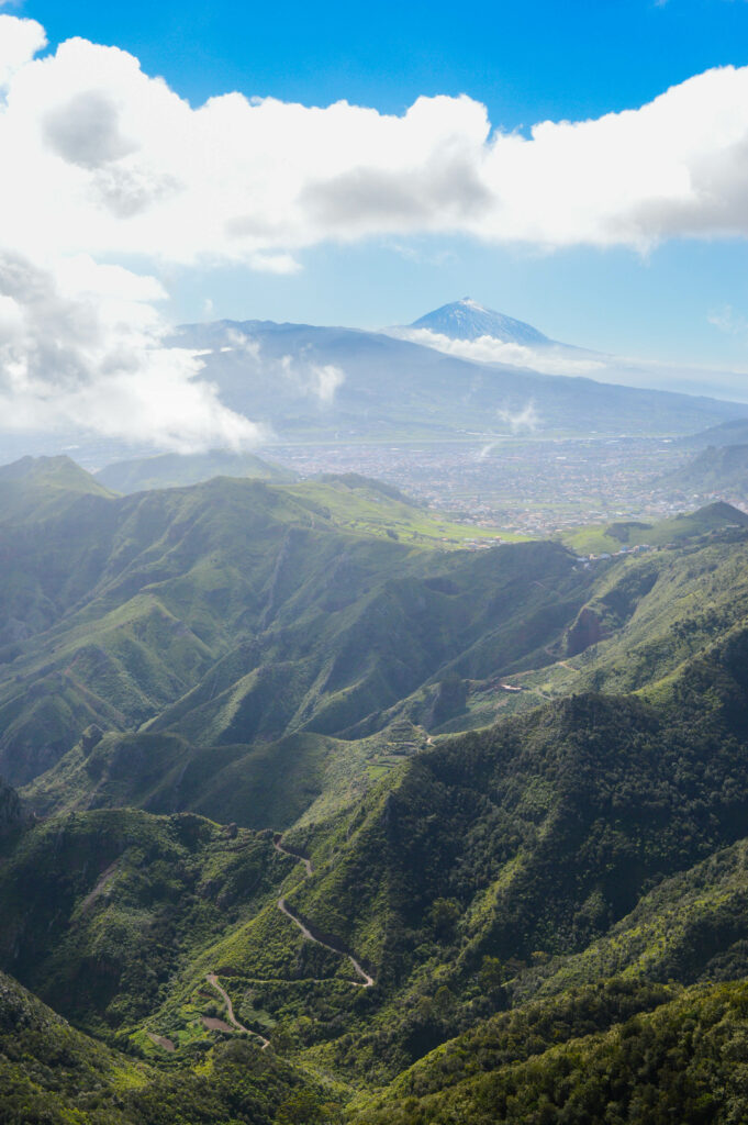 Vue sur la route serpentant au milieu des montagnes vertes de l'Anaga, avec le volcan Teide en arrière plan