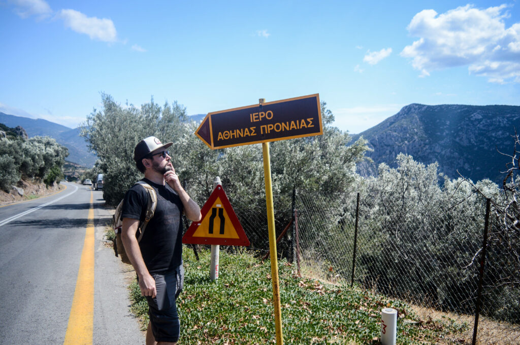 Manu perplexe devant un panneau en bord de route écrit en alphabet grec