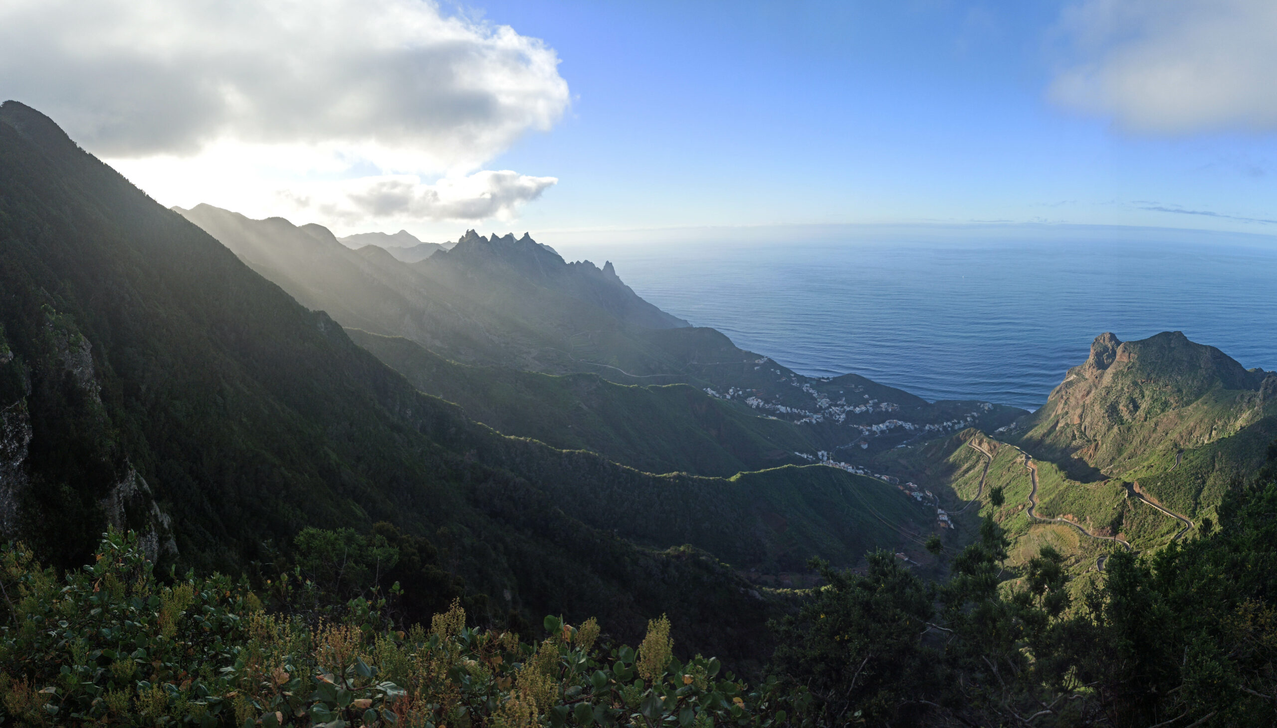 Vue sur les falaises dont dépassent les rayons lumineux du soleil couchant, avec en bas un petit village de Tenerife, au bord de l'océan