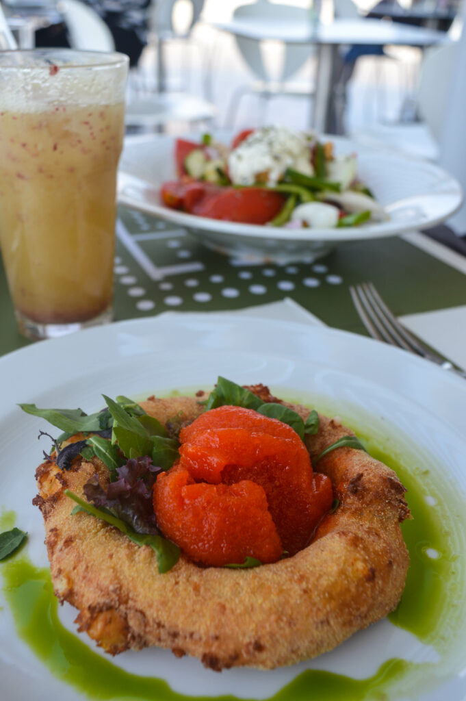 Une assiette avec un Loukoumas : un beignet de feta, rond, pané et frit, contenant en son centre un sorbet de poivron rouge.