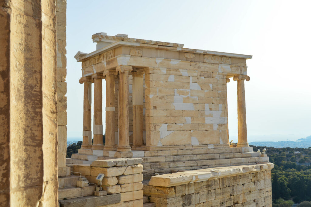 Temple d'Athéna Nikè, petit temple grec antique avec quatre colonnes à l'avant, en pierre claire, situé sur une plate-forme surélevée surplombant le paysage.
