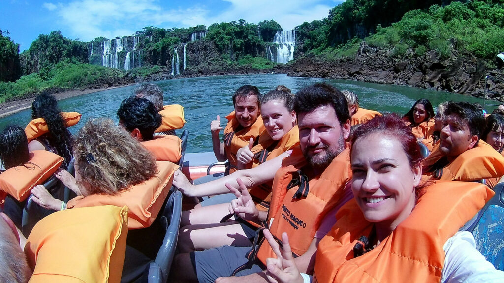 Personnes avec gilet de sauvetage orange, dans un bateau sur la rivière, devant des cascades au loin