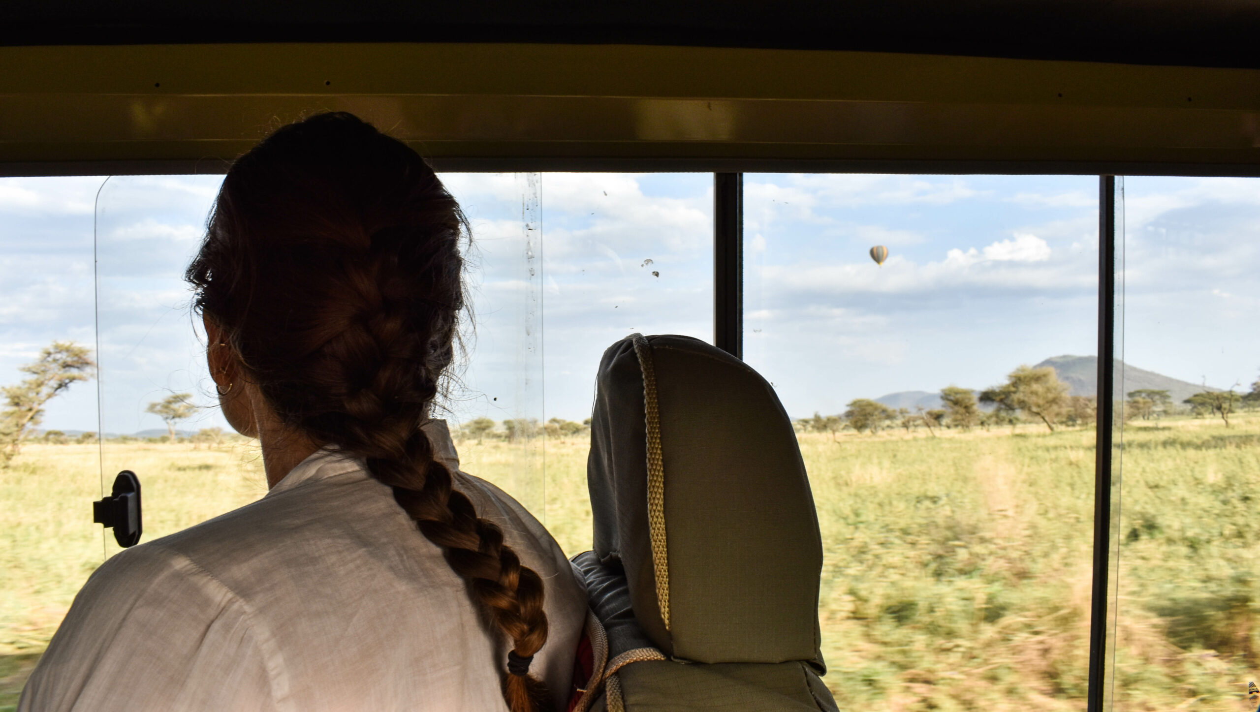 Femme de dos, assise dans un 4x4 lors d'un safari, observant par la fenêtre des montgolfières dans le ciel, au dessus de la savane du Serengeti en Tanzanie