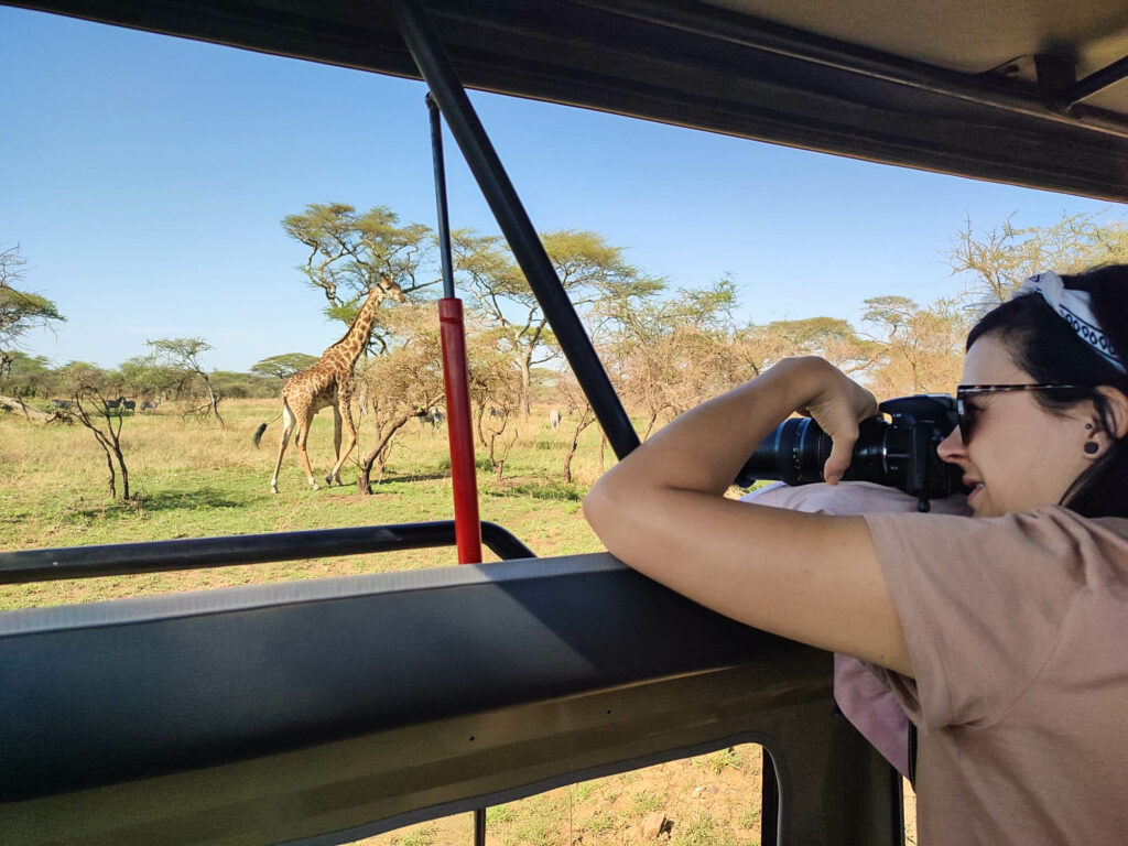 Femme debout dans un 4x4 en train de prendre en photo une girafe sous des acacias, lors d'un safari dans le serengeti en Tanzanie