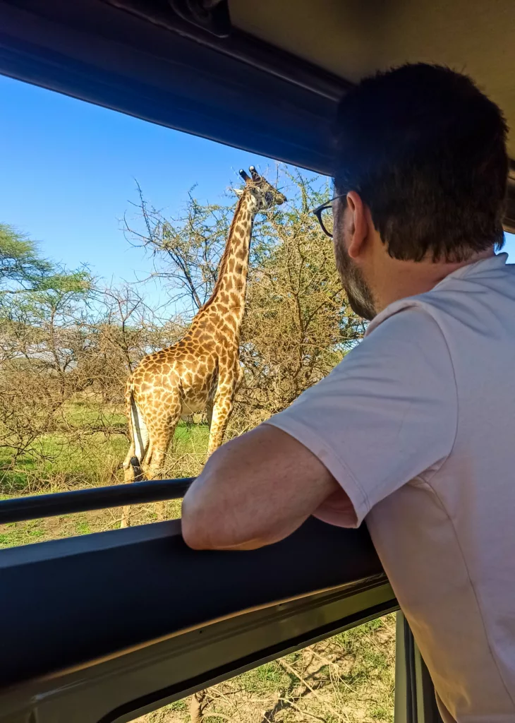 Manu dans le 4x4 regardant une girafe au-dehors, à côté