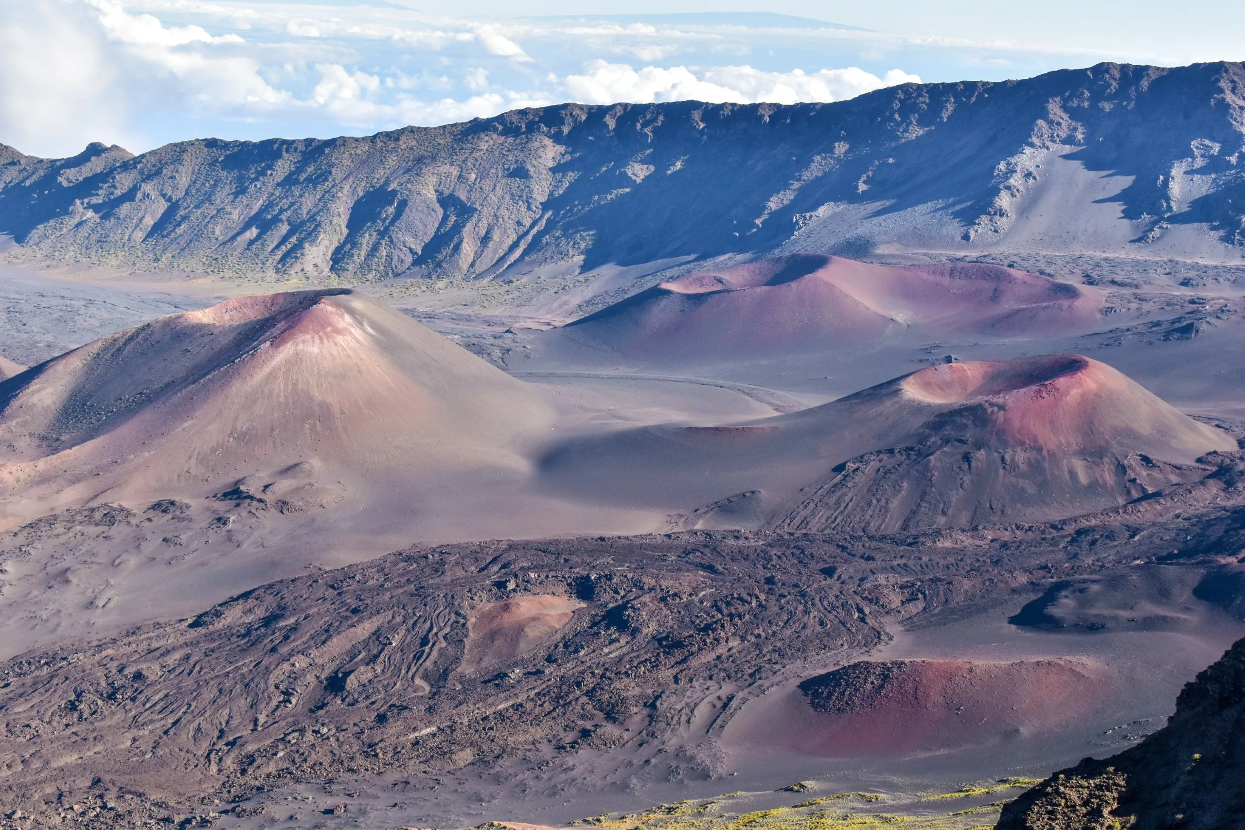 Une vue panoramique du cratère de Haleakalā, avec des cônes de cendres rougeâtres, de la roche volcanique sombre et des parois de cratère accidentées