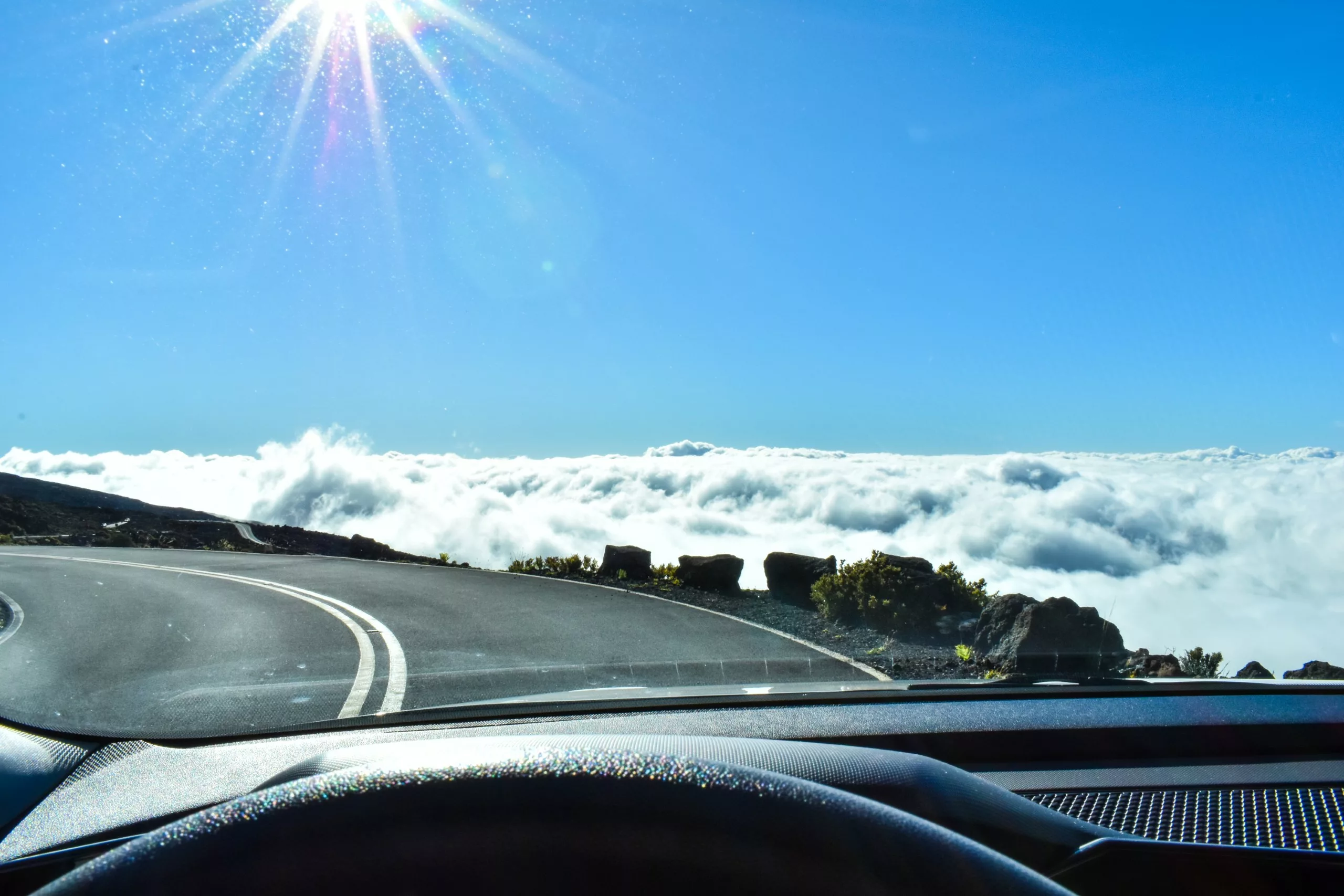 Une route de montagne sinueuse au-dessus des nuages, avec un soleil éclatant et un ciel bleu clair