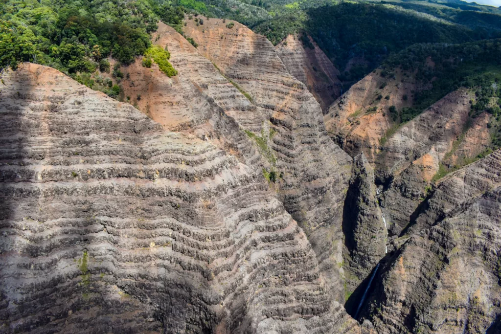 Un paysage présentant des falaises abruptes et accidentées avec des formations rocheuses en couches et des parcelles de végétation