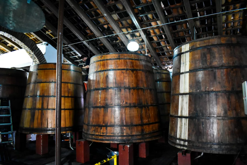 De grandes cuves de fermentation en bois sont alignées sous un toit de tuiles à l'intérieur d'un bâtiment industriel