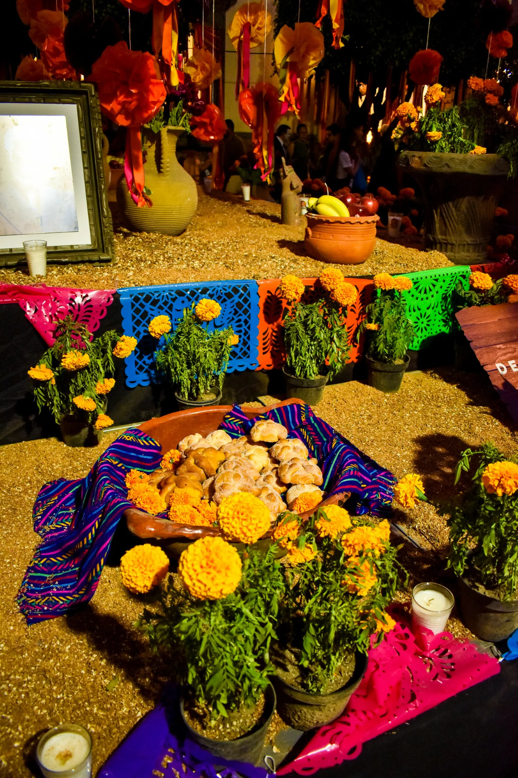 Un autel coloré pour la fête des morts mexicaine présente des fleurs de cempasúchil, des bougies, une photo encadrée, des vases en céramique, du papel picado, des fruits et du pain de muerto sur un tissu décoré.