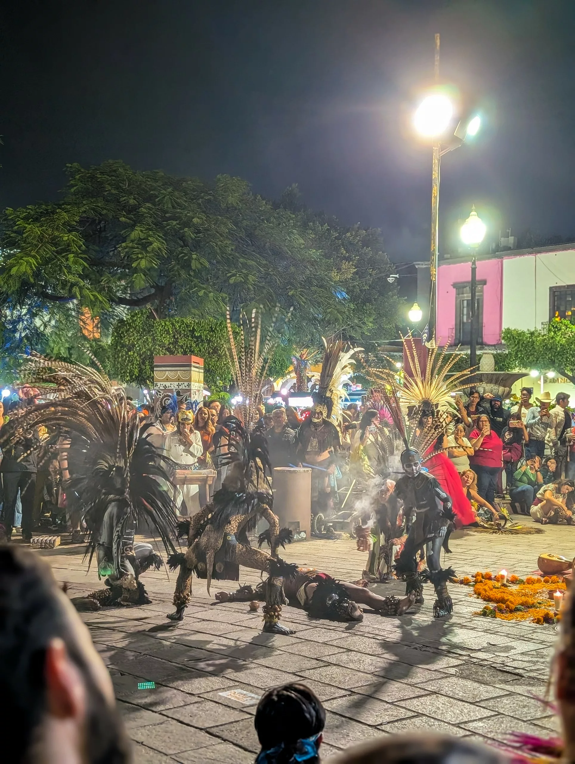 Un groupe de danseurs portant des coiffes traditionnelles à plumes se produit de nuit sur une place publique