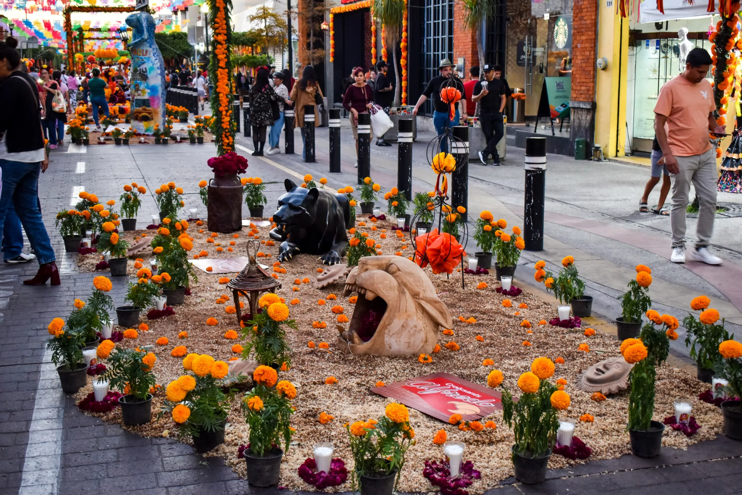 Un autel de rue décoré de fleursi, de bougies, de sculptures et d'offrandes. Des bannières en papel picado lumineux sont suspendues au-dessus