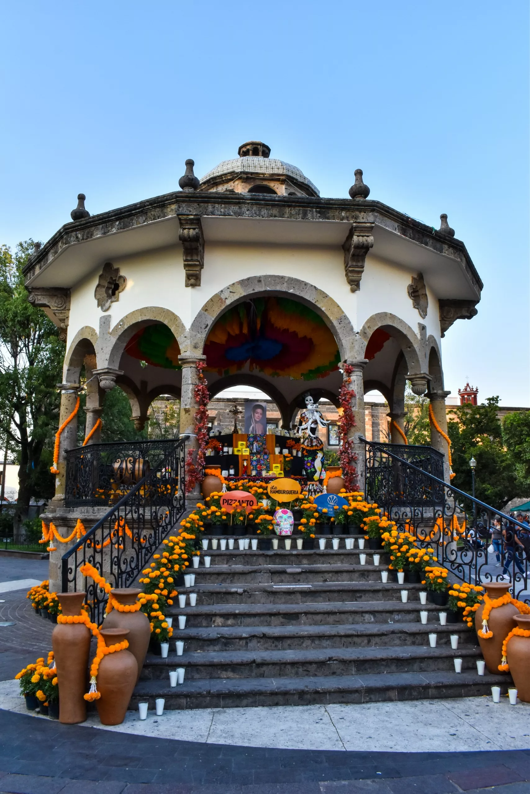Un bâtiment rond décoré de fleurs de soucis, de bougies et de photos forme un autel vibrant pour la fête des morts mexicaine. De grands pots en terre cuite bordent les marches, et des décorations colorées ornent les balustrades et l'intérieur.