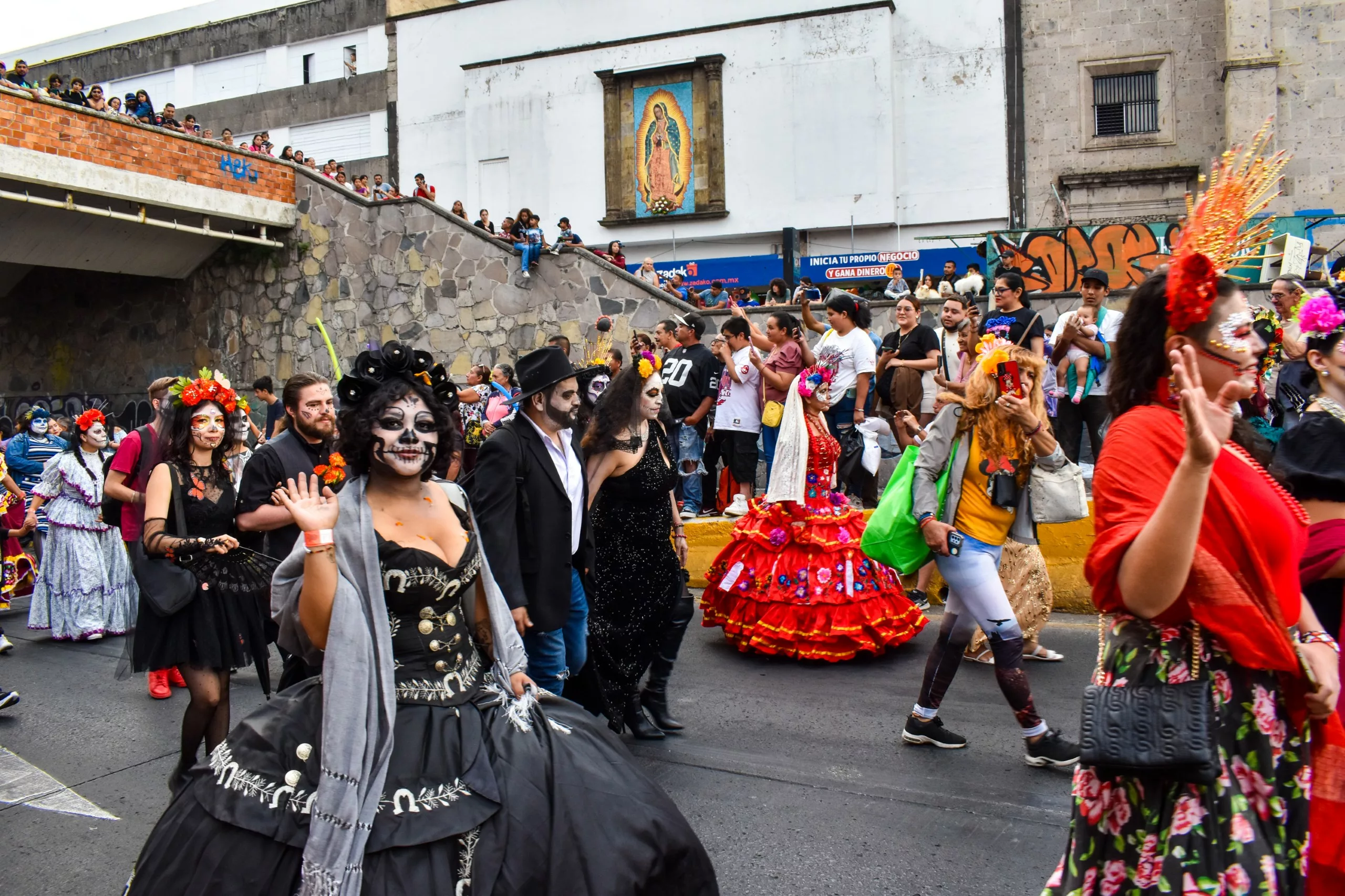 Des personnes vêtues de costumes et maquillées participent à un défilé dans une rue.