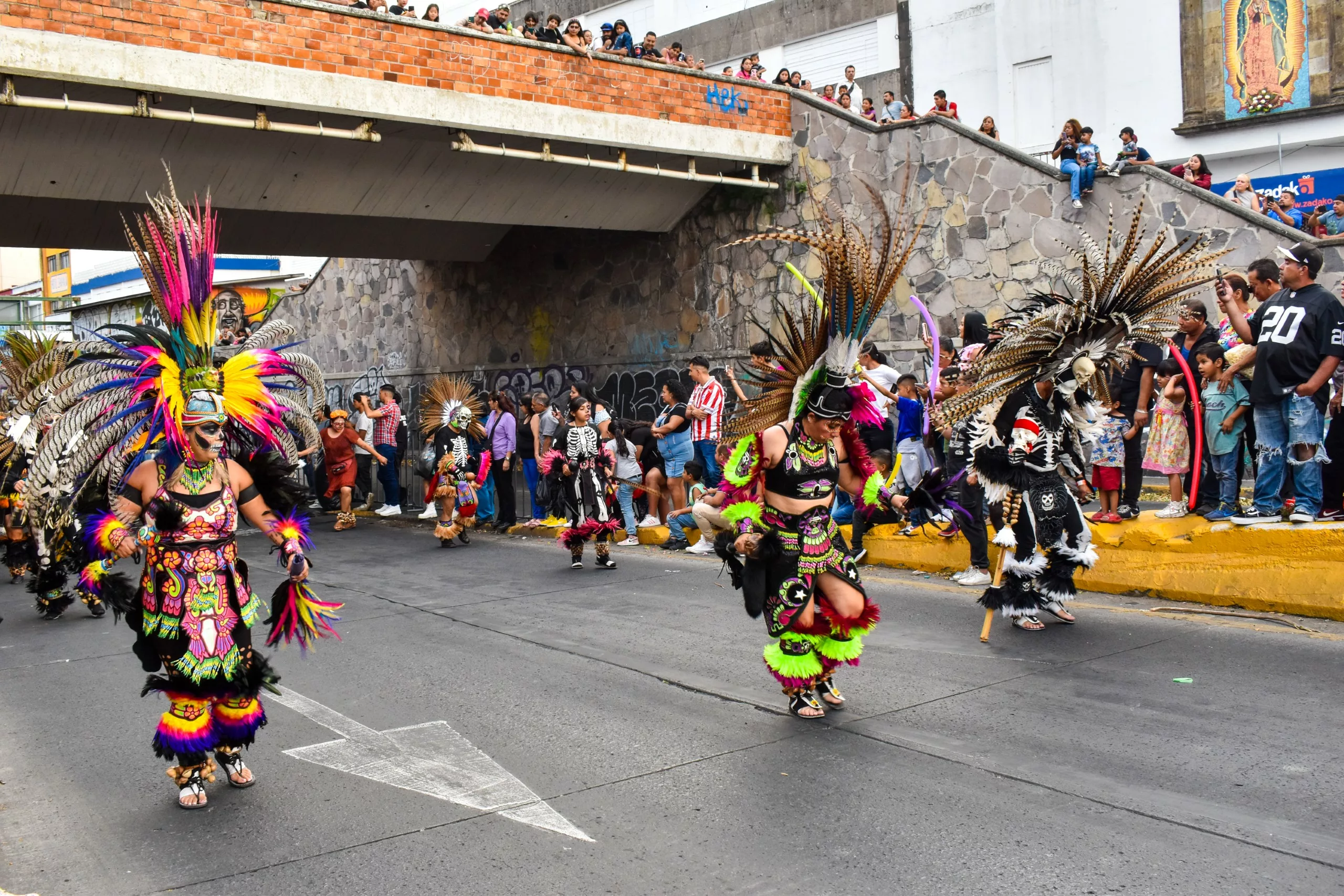 Des personnes vêtues de costumes traditionnels colorés d'inspiration aztèque participent à un défilé de danse de rue.