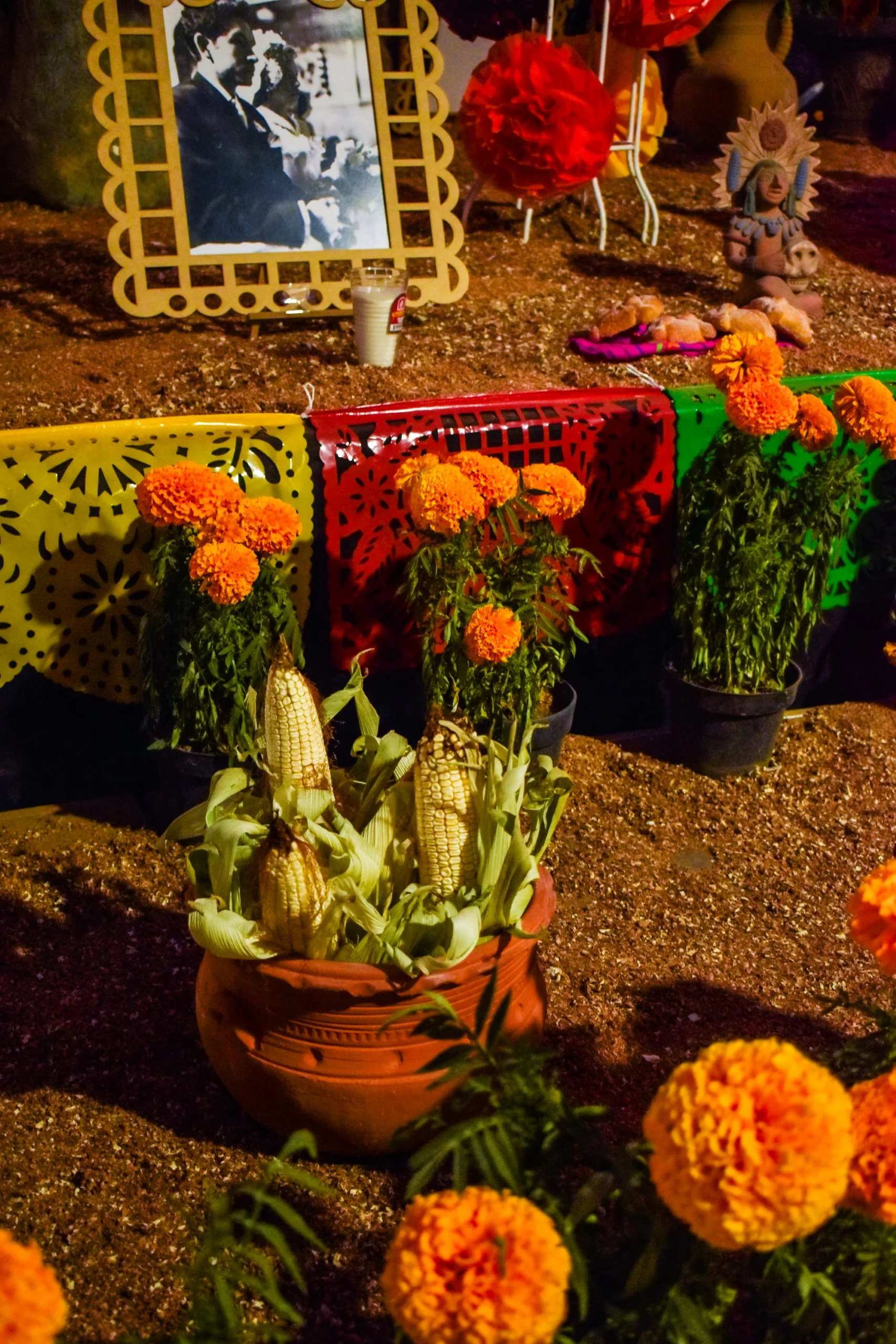 Autel pour la fête des morts mexicaine, orné de fleurs, d'épis de maïs dans un pot en terre cuite, d'une photo en noir et blanc, de papel picado coloré et d'objets traditionnels