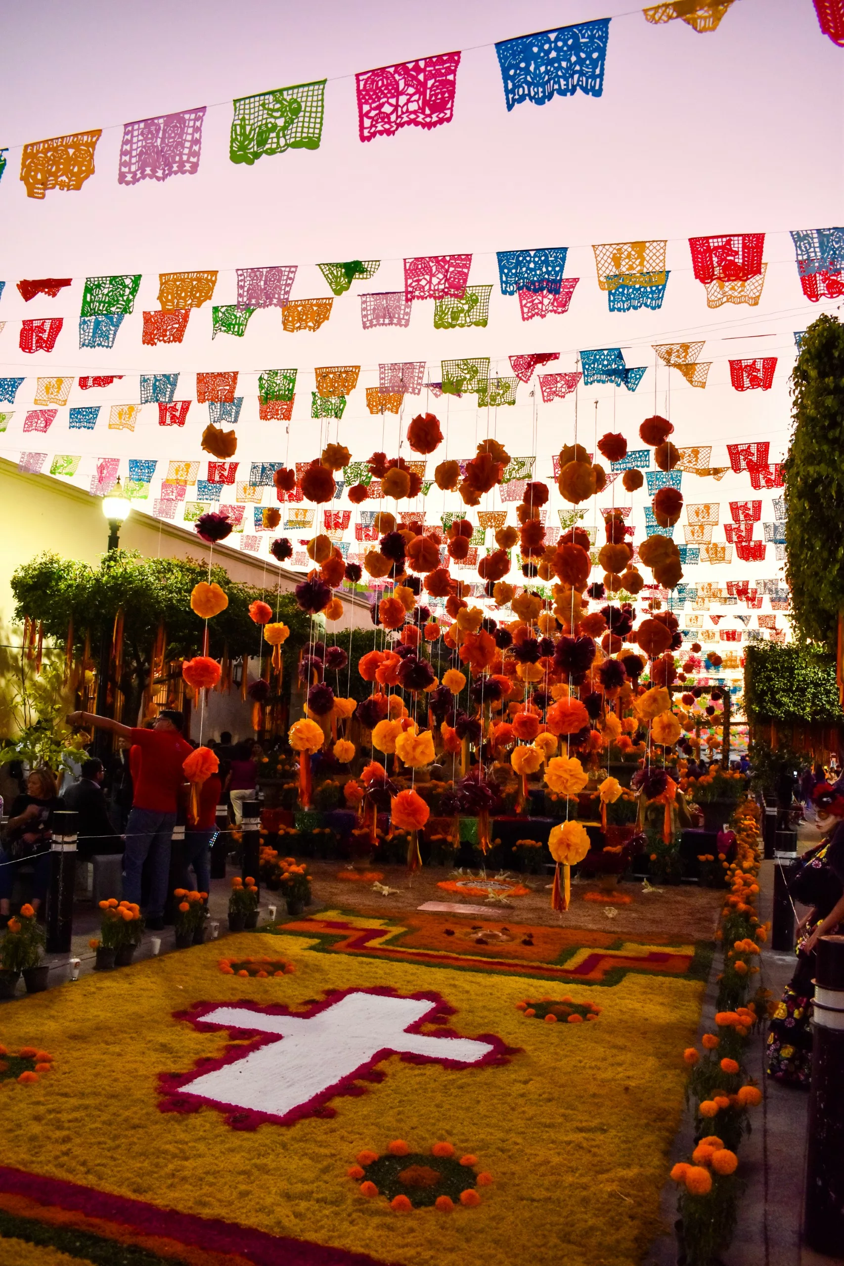 Une rue décorée pour le Día de Muertos, avec des bannières en papel picado, des fleurs oranges et une croix de pétales de fleurs sur le sol.