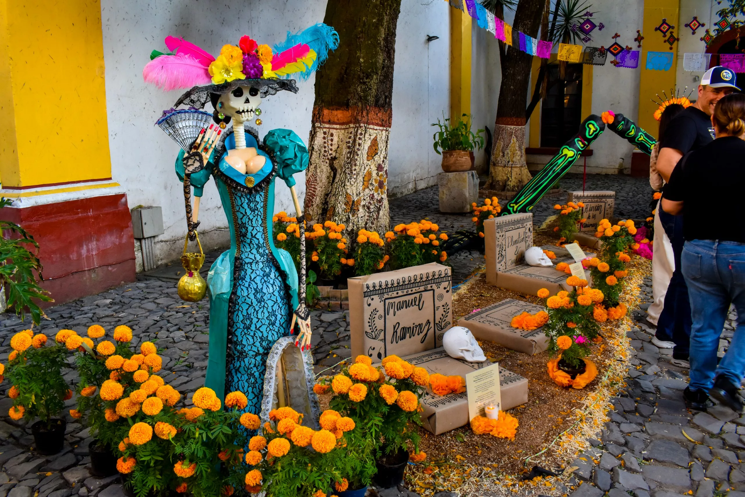 Un autel du Jour des morts pour la fête des morts mexicaine présente des fleurs de cempasúchil, des décorations de pierres tombales, des crânes et un squelette de Catrina vêtu d'une robe bleue et coiffé d'un chapeau à plumes