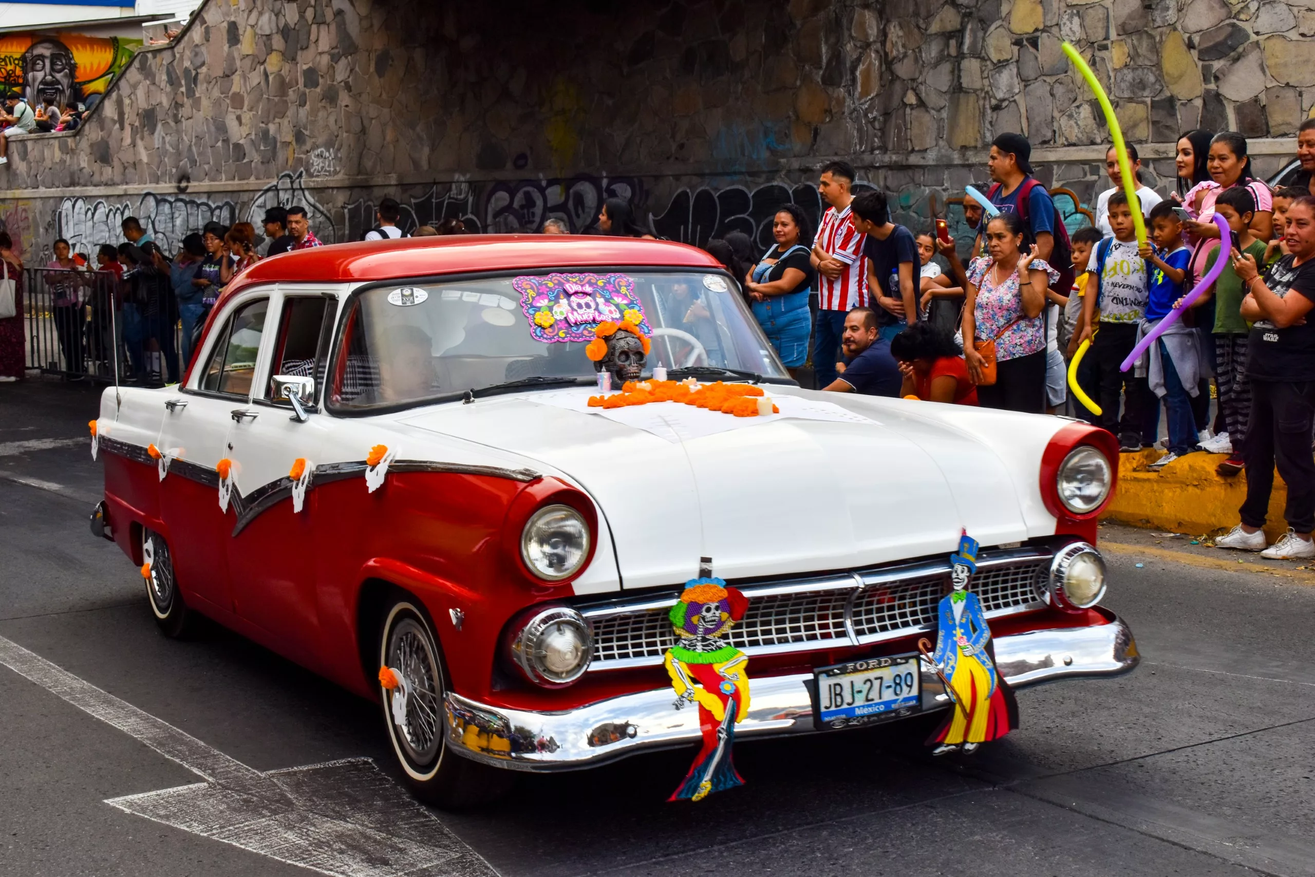 Une voiture de collection rouge et blanche décorée de fleurs orange et de découpages sur le thème de la fête des morts au Mexique participe à un défilé à Guadalajara