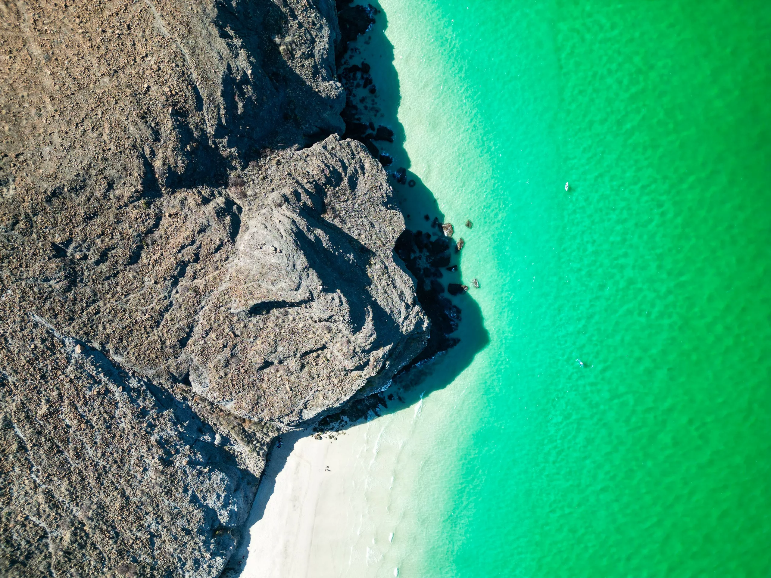Vue aérienne d'une falaise rocheuse rencontrant une plage de sable et une eau turquoise claire
