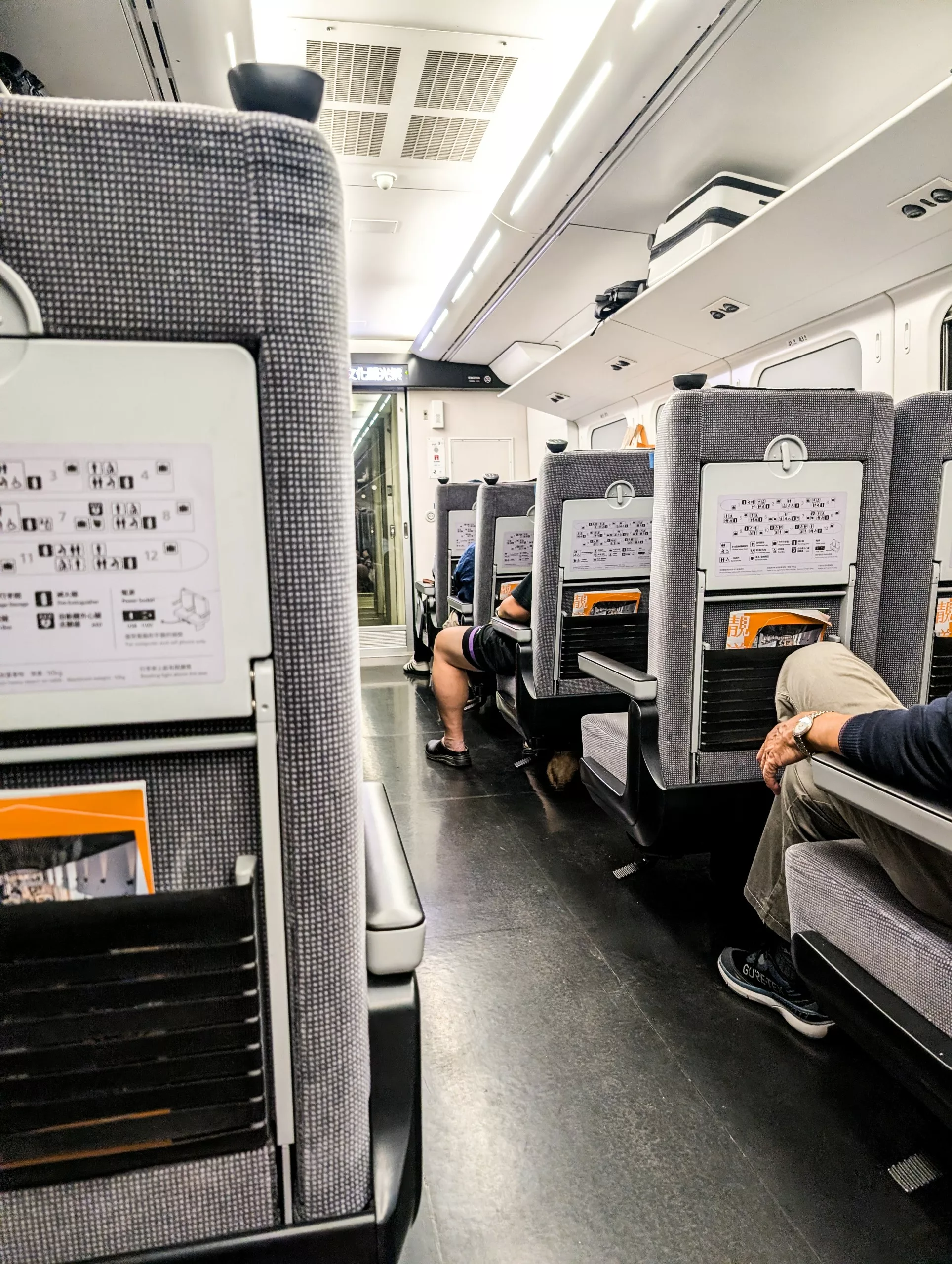L'intérieur d'un train moderne à Taïwan, avec des sièges gris, quelques passagers assis, des porte-bagages au plafond.