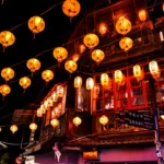 Des rangées de lanternes jaunes incandescentes sont suspendues au-dessus d'une rue animée la nuit à Jiufen, illuminant les bâtiments traditionnels en bois et les fenêtres rouges