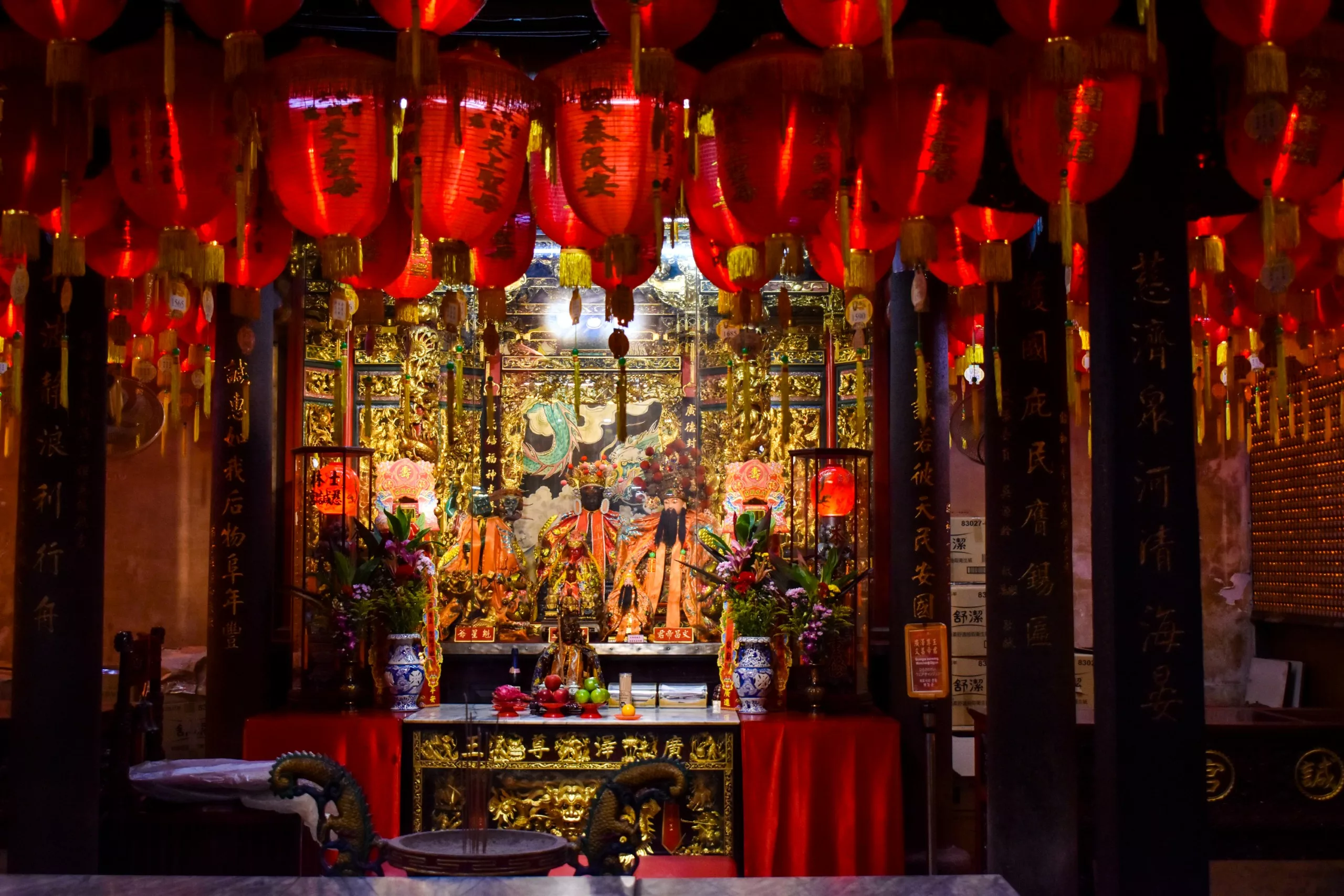 Un autel richement décoré dans un temple chinois, avec des détails dorés, des lanternes rouges avec une écriture noire, des arrangements floraux et des statues religieuses