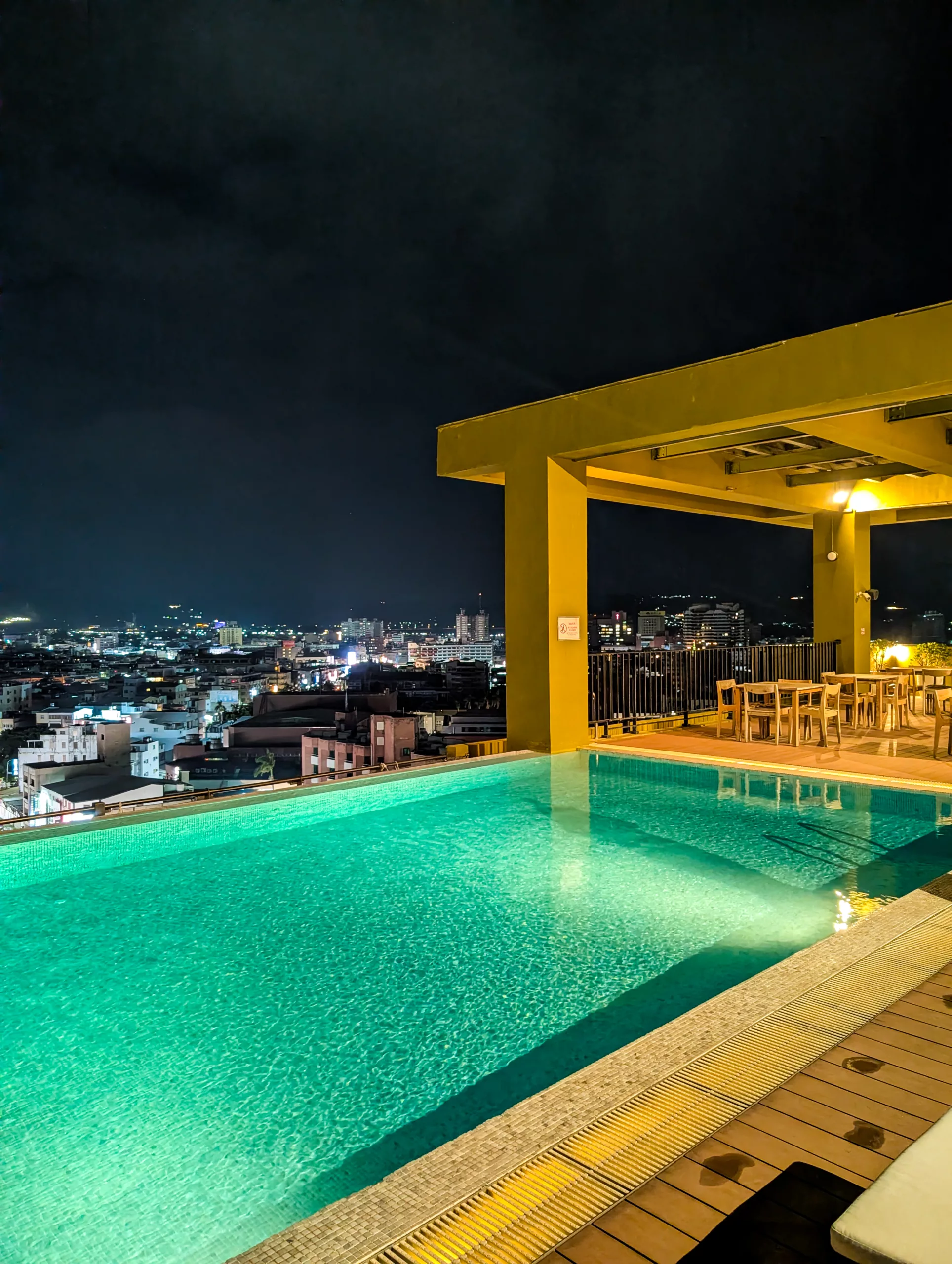 Une piscine à débordement sur un toit surplombe Taitung de nuit, éclairée par des lumières bleu verdâtre.