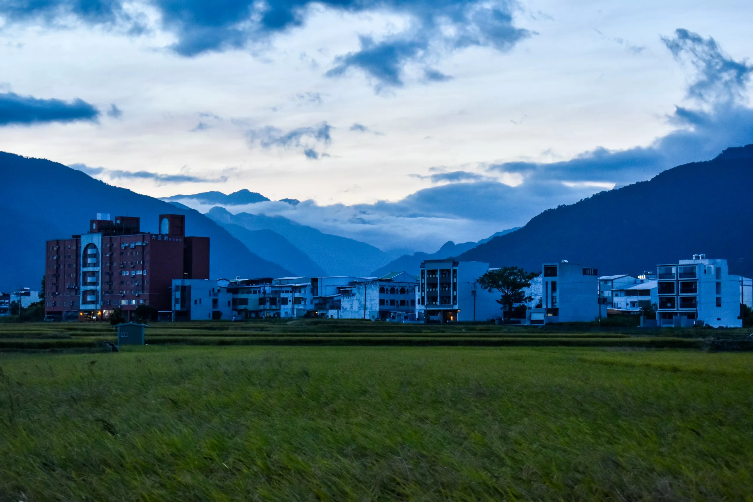 Une architecture moderne se dresse au bord d'un champ, avec des montagnes et un ciel nuageux au crépuscule -